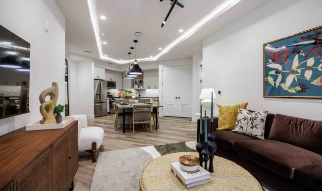 Bright apartment home with an open living, dining, and kitchen layout, showcasing modern finishes, stainless steel appliances, stylish lighting, wood-style flooring, and thoughtfully curated furnishings at The Bouldin.