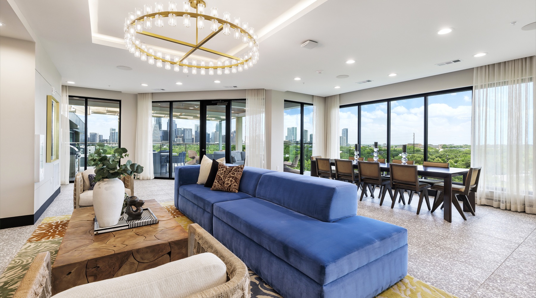 Sophisticated indoor lounge and entertainment space at The Bouldin showcasing modern seating, a large dining table, floor-to-ceiling windows, and sweeping views of downtown Austin from an elevated vantage point.