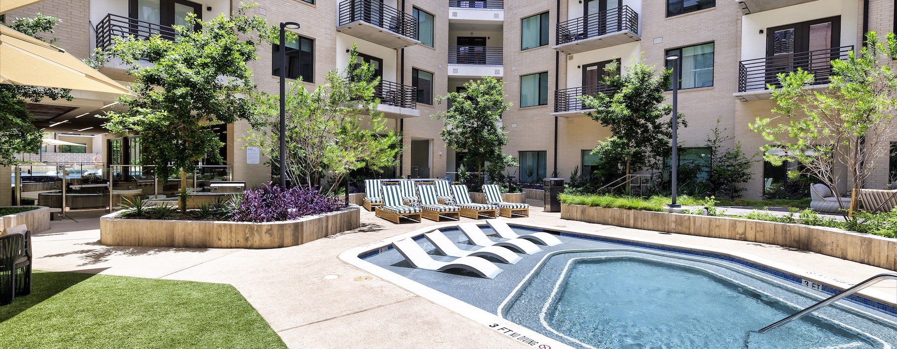 The Bouldin apartment community courtyard featuring two resort-style swimming pools, lounge chairs, shaded seating areas, landscaped greenery, and surrounding residential buildings with private balconies.