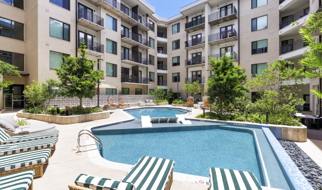 Beautifully landscaped courtyard at The Bouldin showcasing a relaxing pool, fireside lounge, shaded seating areas, outdoor grilling amenities, and contemporary apartment homes with private balconies.