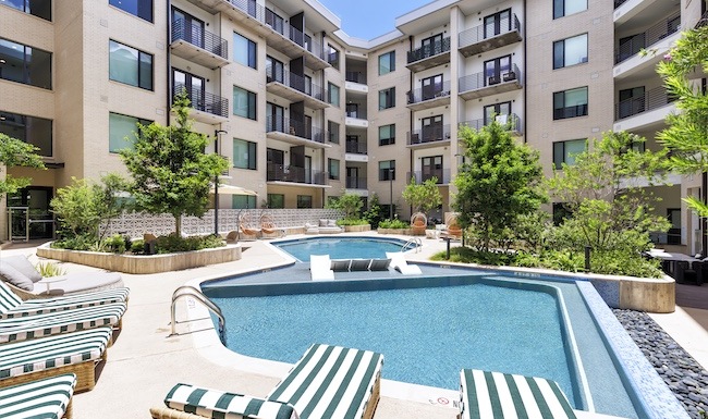 Beautifully landscaped courtyard at The Bouldin showcasing a relaxing pool, fireside lounge, shaded seating areas, outdoor grilling amenities, and contemporary apartment homes with private balconies.